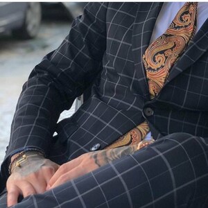 Puede incluir: Un hombre con un traje azul oscuro, camisa blanca y corbata con estampado paisley. El traje tiene un sutil estampado a cuadros.