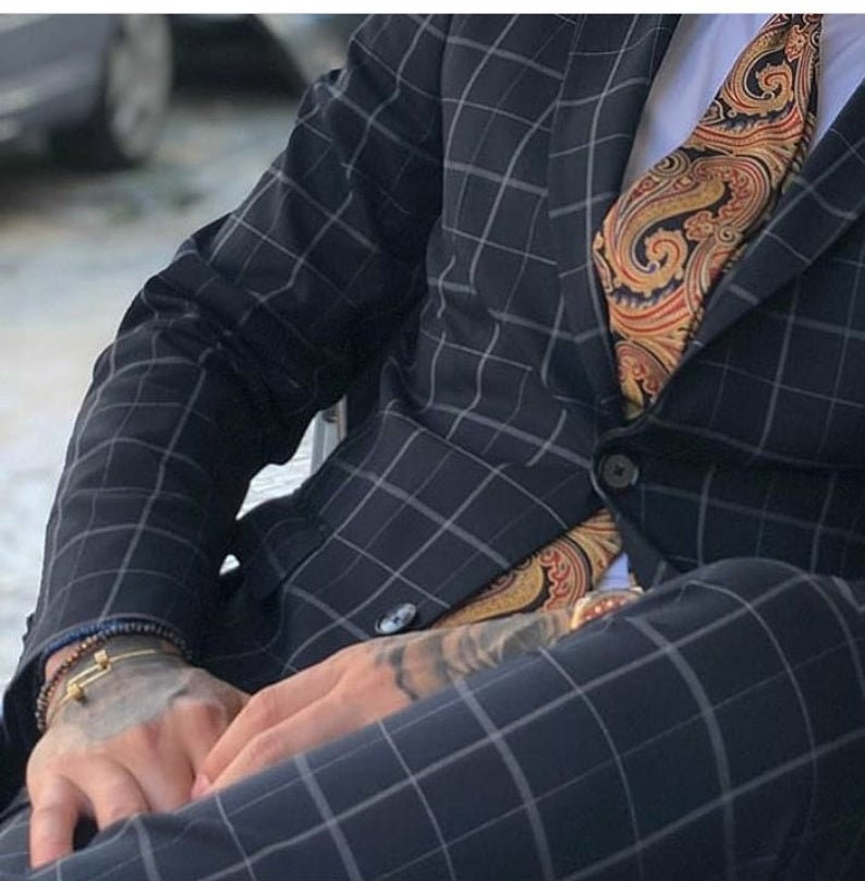 Puede incluir: Un hombre con un traje azul oscuro, camisa blanca y corbata con estampado paisley. El traje tiene un sutil estampado a cuadros.