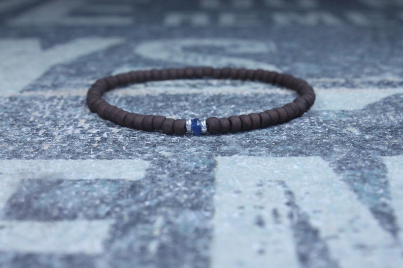 Puede incluir: Un brazalete de cuentas marrones con un solo acento de piedra preciosa azul.