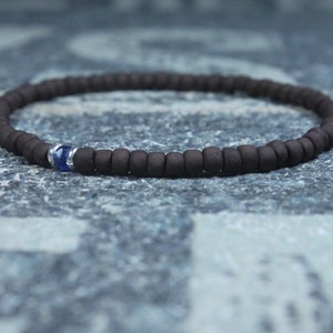 Puede incluir: Un brazalete de cuentas marrones con un solo acento de piedra preciosa azul.