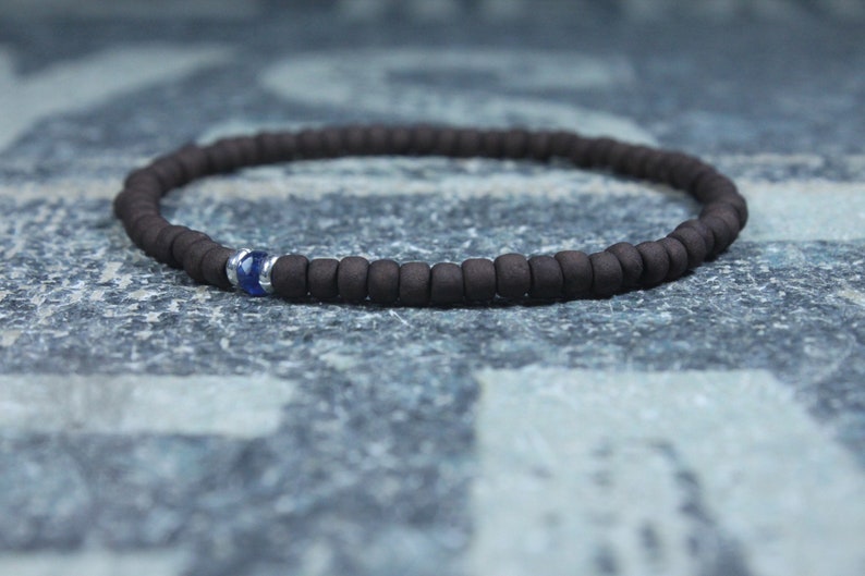 Puede incluir: Un brazalete de cuentas marrones con un solo acento de piedra preciosa azul.
