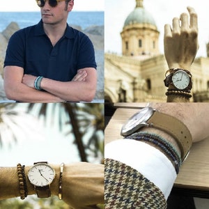 May include: A close-up of a wrist with a silver watch and a brown leather band. The watch has a white face with black hands and black Roman numeral markings. The wrist is wearing multiple bracelets, including a beaded bracelet, a brown leather bracelet, and a gold bracelet.