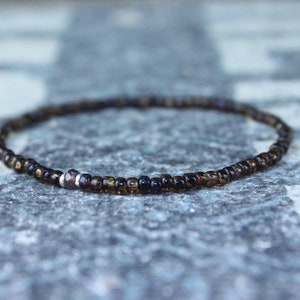 May include: A delicate brown and black beaded bracelet with a silver bead accent.