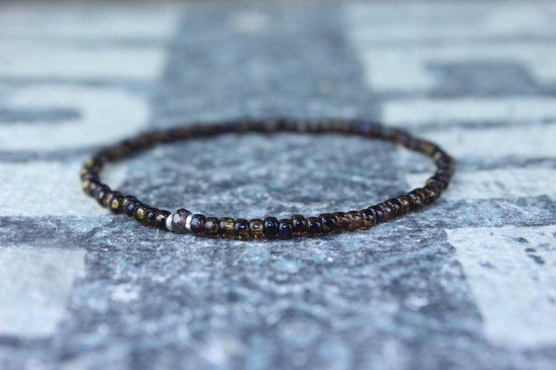 May include: A delicate brown and black beaded bracelet with a silver bead accent.
