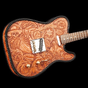 Może przedstawiać: Brązowa skórzana gitara elektryczna z misternymi, tłoczonymi wzorami, w tym czaszką, kwiatami i gwiazdą szeryfa. Gitara ma czarną skórzaną obwódkę i srebrny pickguard.