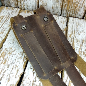 May include: Brown leather phone holster with two straps and metal snaps. The holster is designed to be worn on a belt.