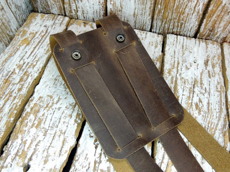 May include: Brown leather phone holster with two straps and metal snaps. The holster is designed to be worn on a belt.