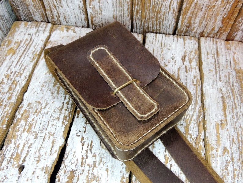 May include: A brown leather crossbody bag with a flap closure and a white stitching detail. The bag has a brass buckle and a brown leather strap.