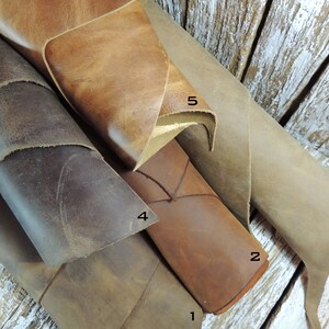 May include: Five different pieces of leather in various shades of brown, tan, and gray. The leather is rolled up and arranged in a pile. The leather is numbered 1 through 5.
