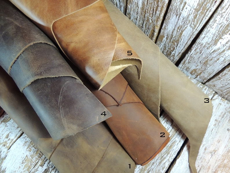 May include: Five different pieces of leather in various shades of brown, tan, and gray. The leather is rolled up and arranged in a pile. The leather is numbered 1 through 5.