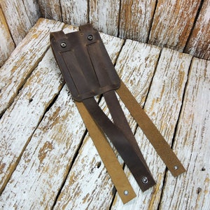 May include: A brown leather phone holster with three straps. The holster has two metal snaps and is designed to be worn on a belt.