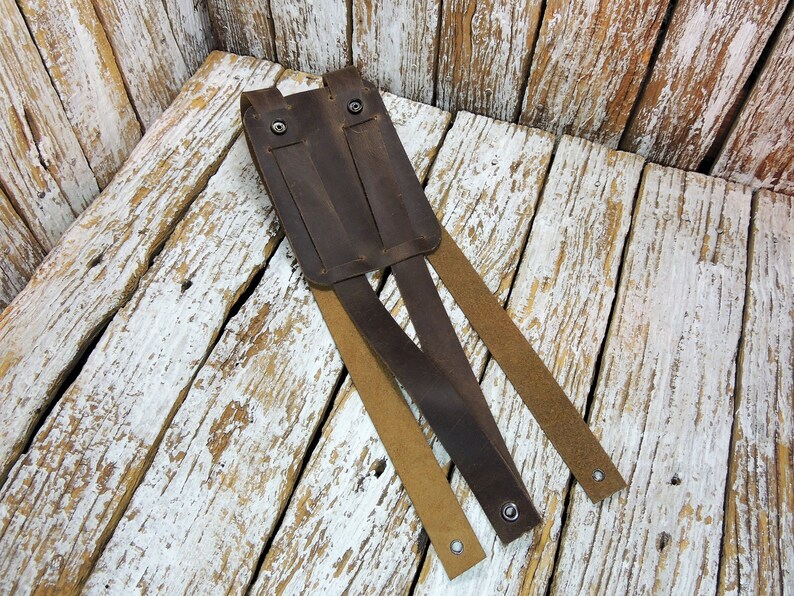 May include: A brown leather phone holster with three straps. The holster has two metal snaps and is designed to be worn on a belt.