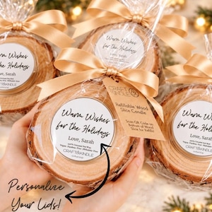 May include: Four round wood slice candles wrapped in clear plastic with gold satin ribbons. Each candle features a white circular label with the text Warm Wishes for the Holidays, Love, Sarah, and Craft & Kindle. One candle includes a tag with instructions.