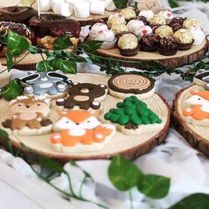 Puede incluir: Un plato de madera con una variedad de galletas de az&uacute;car decoradas con animales del bosque, incluyendo un mapache, un oso, un ciervo, un zorro y un pino. Las galletas est&aacute;n dispuestas en un plato de madera con un dise&ntilde;o de tronco de &aacute;rbol.