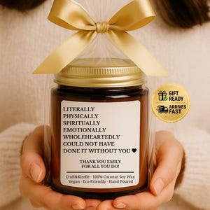 May include: A candle in a glass jar with a gold lid, wrapped in cellophane and tied with a gold ribbon. The label reads "Literally, Physically, Spiritually, Emotionally, Wholeheartedly, Could Not Have Done It Without You. Thank You Emily For All You Do!"