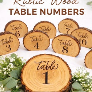 May include: Rustic wood table numbers. The image shows several wooden table number signs, each cut from a tree slice. The numbers are printed in black, with the word "Table" above each number. The signs are surrounded by greenery.
