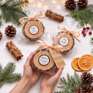 May include: Three round wood slice candles wrapped in clear plastic with beige ribbons. The labels read Fraser Fir, Cozy Vanilla, and Apples & Cinnamon. A brown tag attached to the front candle reads Craft Kindle Refillable Wood Slice Candle.