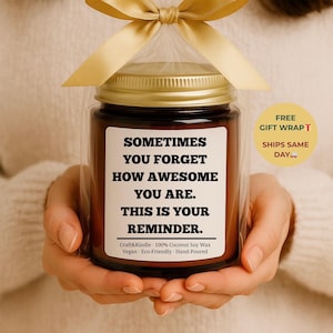 May include: A brown glass jar candle with a gold lid, wrapped in clear cellophane and tied with a gold ribbon. The label reads "SOMETIMES YOU FORGET HOW AWESOME YOU ARE. THIS IS YOUR REMINDER."
