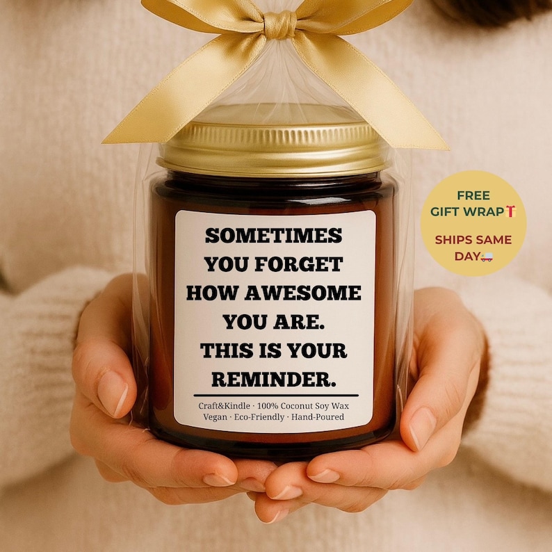 May include: A brown glass jar candle with a gold lid, wrapped in clear cellophane and tied with a gold ribbon. The label reads "SOMETIMES YOU FORGET HOW AWESOME YOU ARE. THIS IS YOUR REMINDER."