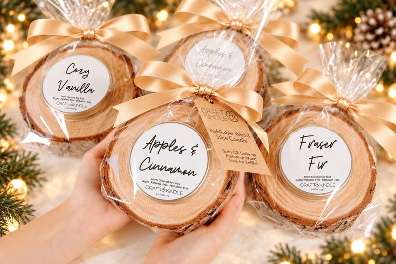 May include: Four refillable wood slice candles packaged in clear plastic with gold ribbons. Each candle features a white label with black text including scent names like Cozy Vanilla, Apples & Cinnamon, and Fraser Fir, plus the Craft & Kindle brand name.