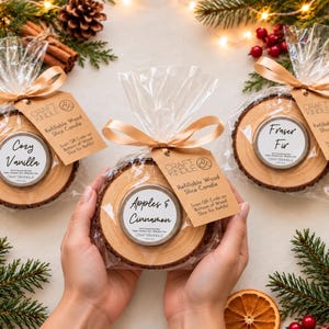 May include: Three refillable wood slice candles in clear plastic bags with gold ribbons and brown tags. The labels read Cozy Vanilla, Apples & Cinnamon, and Fraser Fir. Each candle is set in a natural wood slice with bark edges.