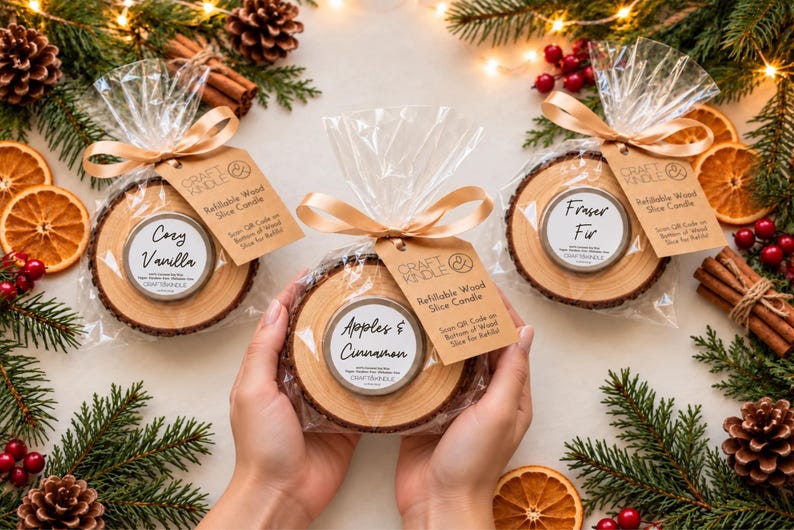 May include: Three refillable wood slice candles in clear plastic bags with gold ribbons and brown tags. The labels read Cozy Vanilla, Apples & Cinnamon, and Fraser Fir. Each candle is set in a natural wood slice with bark edges.