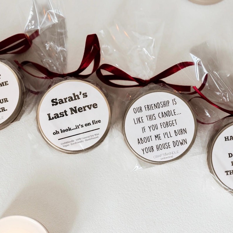 Puede incluir: Varias velas peque&ntilde;as y redondas en bolsas de celof&aacute;n transparente atadas con cintas color burdeos. Las etiquetas de las velas presentan frases humor&iacute;sticas.