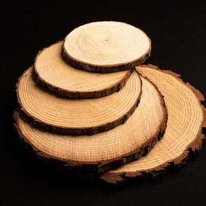 May include: A stack of six round wooden coasters with visible growth rings and natural bark edges. The coasters are arranged in a cascading pattern against a black background, showcasing their light brown color and rustic texture.