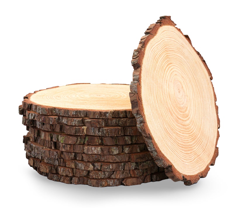 May include: A stack of wooden round slices with bark edges. The slices are arranged in a staggered pattern, with the top slice slightly offset from the others. The wood is a light brown color with a natural grain pattern.