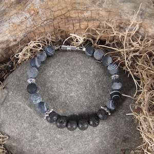 May include: A black and gray beaded bracelet with a silver clasp. The bracelet is made with agate and lava rock beads.
