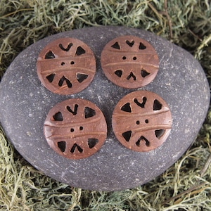 May include: Four brown wooden buttons with a geometric design. The buttons have a carved pattern and two holes in the center.
