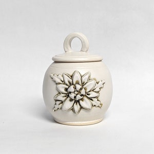 May include: White ceramic jar with a lid and a floral design. The jar has a handle on the lid.