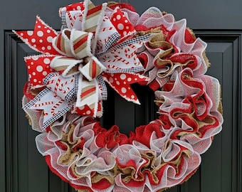 May include: A red, white, and brown Christmas wreath with a large bow made of red and white polka dot fabric, white and red striped fabric, and white fabric with a candy cane print. The wreath is made of burlap and white mesh.