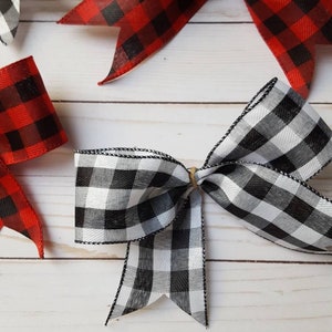 May include: Overhead shot of several decorative bows in red and black buffalo plaid and black and white gingham patterns. The bows are tied with twine and have wired edges. The bows are arranged on a light wood grain surface.