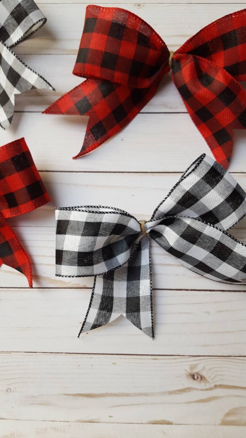 May include: Overhead shot of several decorative bows in red and black buffalo plaid and black and white gingham patterns. The bows are tied with twine and have wired edges. The bows are arranged on a light wood grain surface.