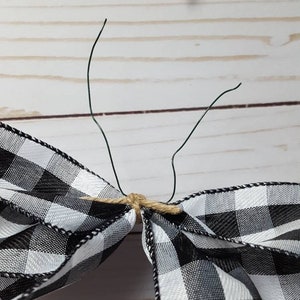 May include: A close-up of a black and white checkered bow with green wire stems. The bow is tied with twine. A red and black checkered bow is in the background. The bows are likely for crafting or decoration.