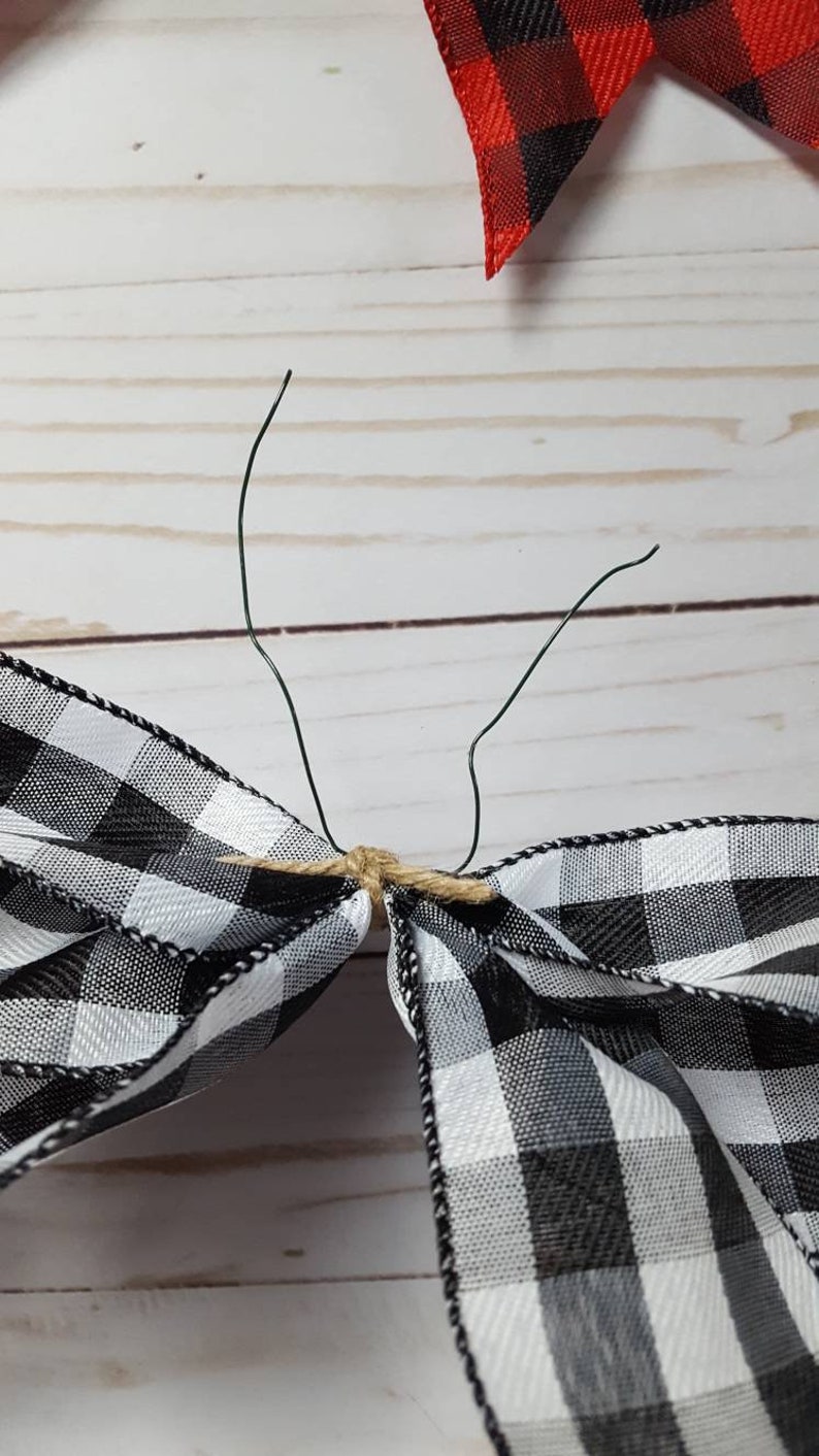 May include: A close-up of a black and white checkered bow with green wire stems. The bow is tied with twine. A red and black checkered bow is in the background. The bows are likely for crafting or decoration.
