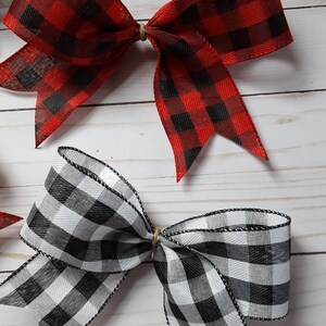 May include: Two decorative bows, one red and black buffalo plaid, the other black and white. The bows are tied with twine and have a classic, rustic aesthetic. The fabric has a woven texture.