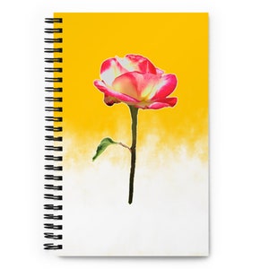 May include: A spiral-bound notebook with a rose design. The cover displays a red and white rose set against a yellow and white gradient. The notebook's design is simple and elegant, suitable for note-taking or journaling.
