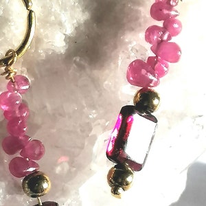 Könnte beinhalten: Goldkette mit rosafarbenen und roten Edelsteinperlen. Die Kette hat oben einen kleinen goldenen Ring.