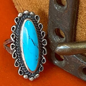 Puede incluir: Un anillo de plata con una piedra turquesa engastada en forma ovalada. El anillo est&aacute; decorado con un dise&ntilde;o de filigrana de plata.
