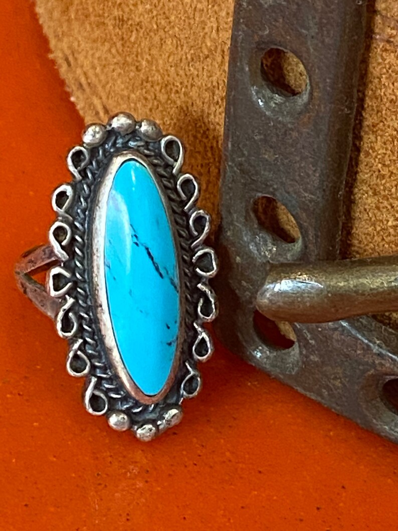 Puede incluir: Un anillo de plata con una piedra turquesa engastada en forma ovalada. El anillo est&aacute; decorado con un dise&ntilde;o de filigrana de plata.