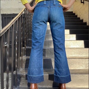 Pu&ograve; includere: Un paio di jeans blu denim a gamba larga con orlo a pie rovesciato. I jeans hanno vita alta e chiusura con bottone.