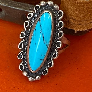 Puede incluir: Un anillo de plata con una piedra turquesa engastada en forma ovalada. El anillo est&aacute; decorado con un dise&ntilde;o de filigrana de plata.