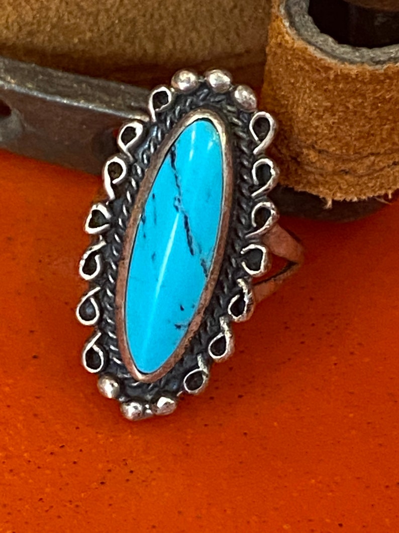 Puede incluir: Un anillo de plata con una piedra turquesa engastada en forma ovalada. El anillo est&aacute; decorado con un dise&ntilde;o de filigrana de plata.