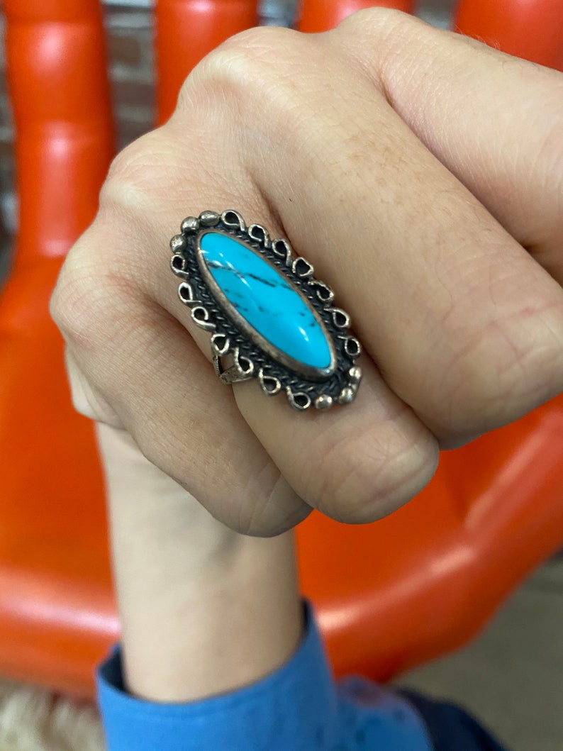 Puede incluir: Un anillo de plata con una piedra ovalada turquesa engastada en un marco decorativo de plata.