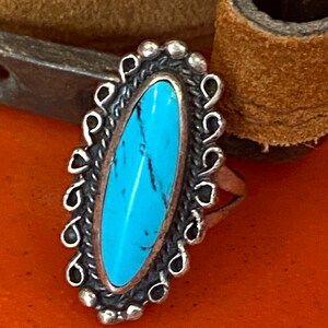 Puede incluir: Un anillo de plata con una piedra turquesa engastada en forma ovalada. El anillo tiene un borde decorativo alrededor de la piedra.