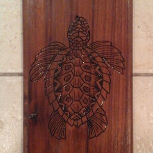 May include: A dark brown wooden plaque with a black sea turtle design burned into the surface. The turtle has a detailed shell and flippers.