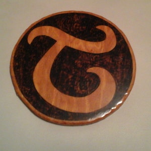 May include: A wooden round plaque with a black stylized letter "T" in the center.