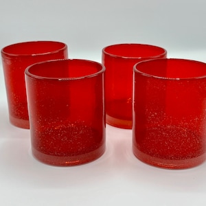 May include: Four red glass tumblers with a speckled texture. The tumblers are all the same size and shape.